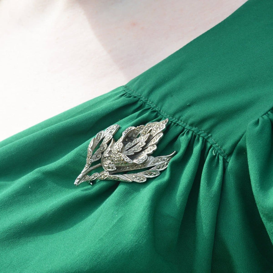 1940s chrome and marcasite floral brooch on green dress, showcasing intricate design and classic vintage elegance.