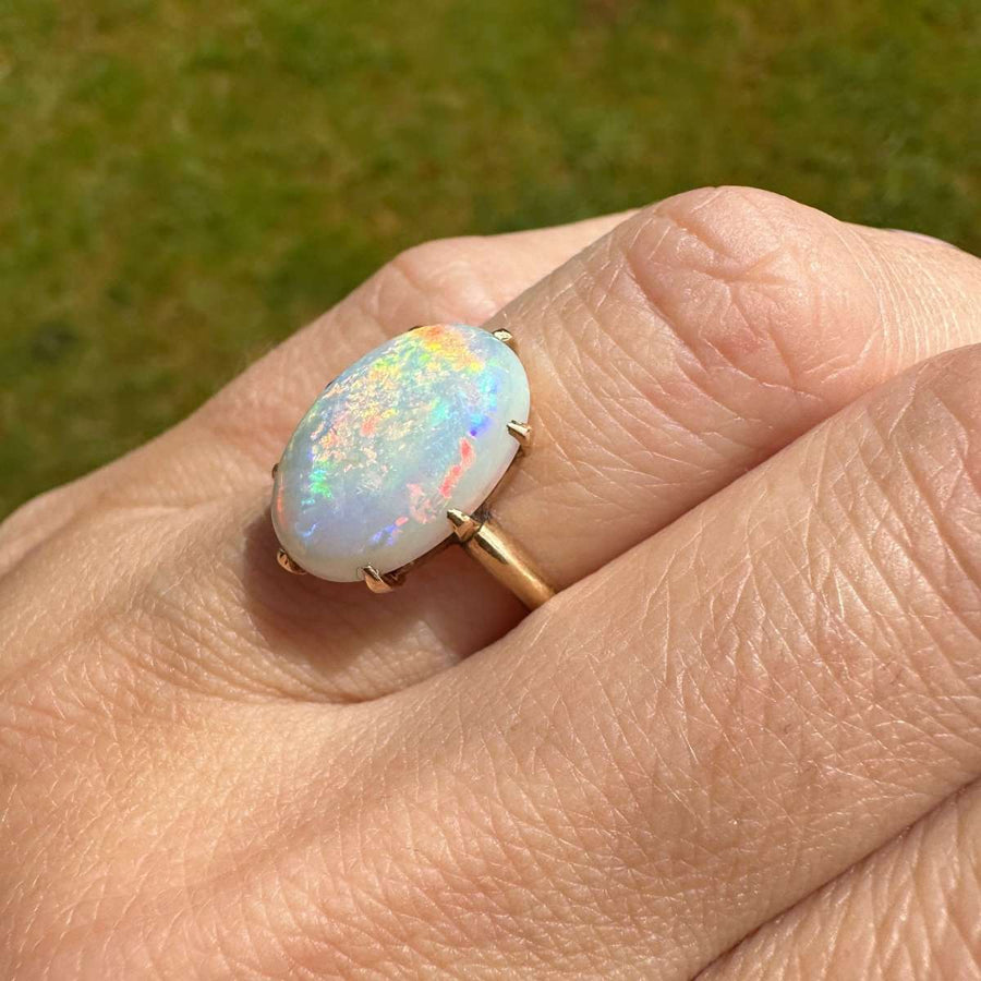 Art Deco 18ct gold ring with white opal displaying vivid red and colorful flashes on a hand.