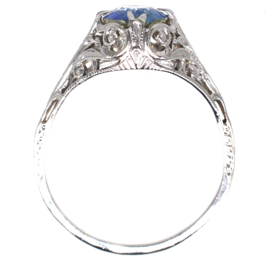 Belle Époque 18ct white gold ring featuring a cornflower blue sapphire and intricate foliate scroll design.