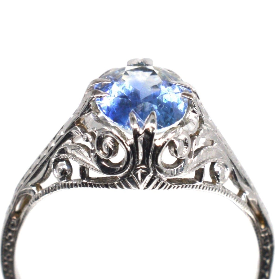 Belle Époque 18ct white gold ring featuring a cornflower blue sapphire and intricate foliate scroll design.