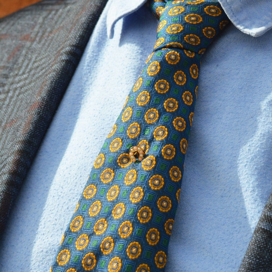 Close-up of a patterned tie featuring vibrant blue and gold floral designs, worn on a textured suit.