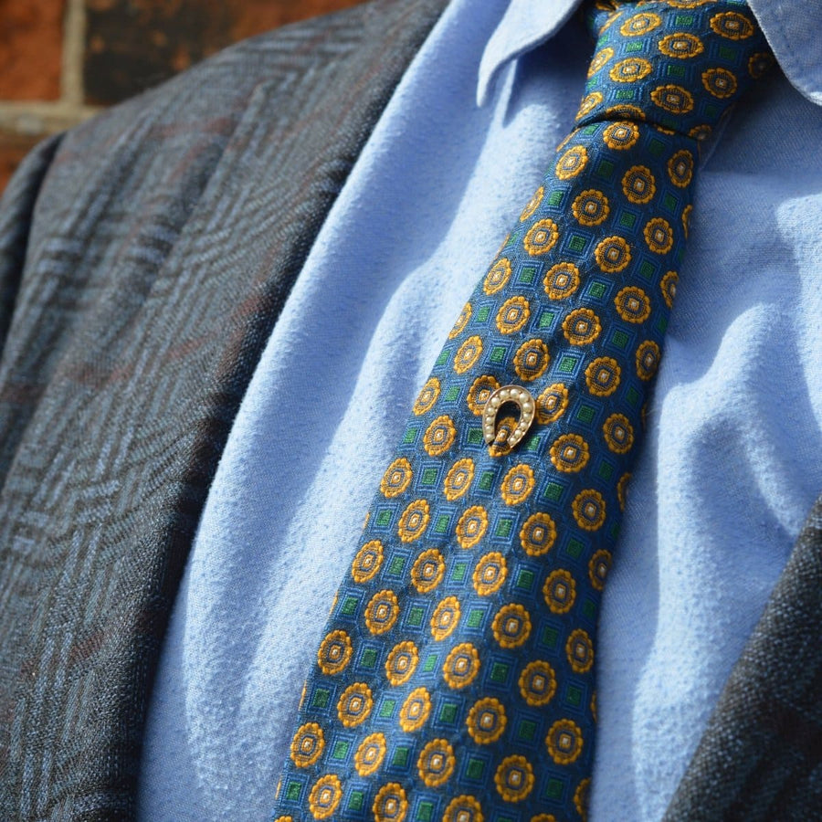 Late Victorian 9ct gold seed pearl horseshoe tie pin on a patterned tie, symbolizing good luck and style.