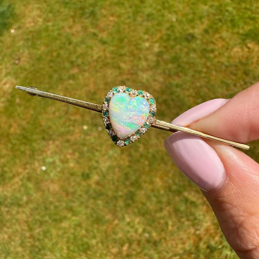 Victorian gold bar brooch featuring a heart-shaped opal surrounded by diamonds and emeralds.