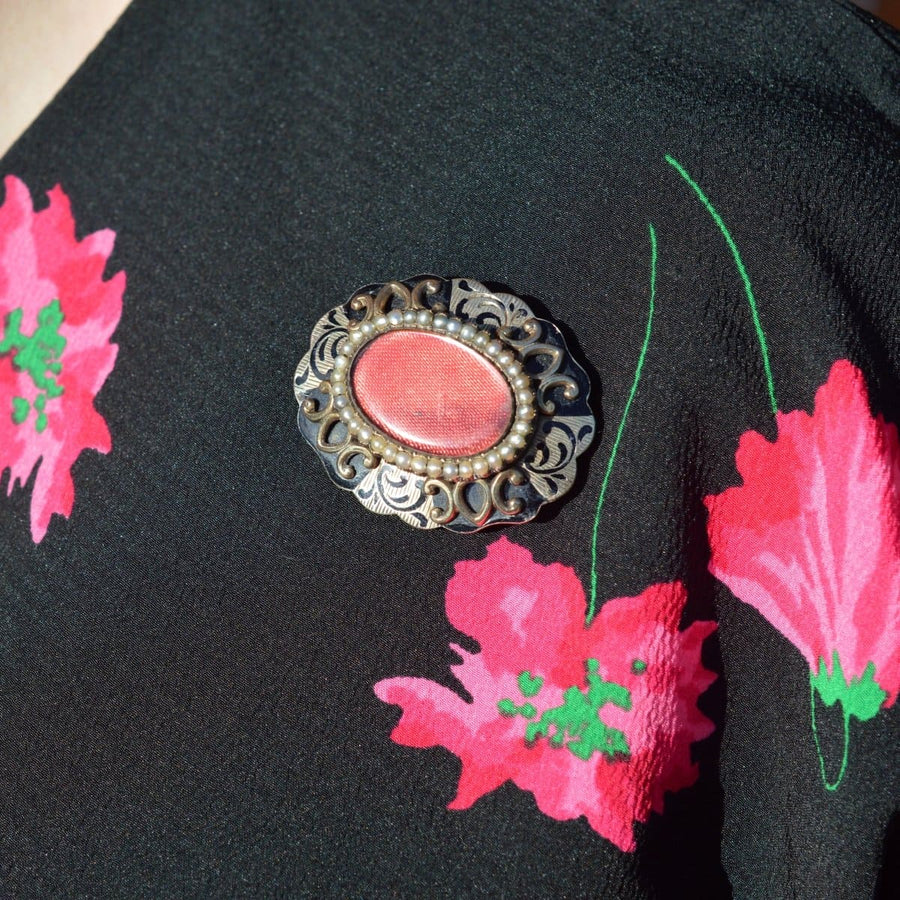 Victorian brooch with ornate design and red center worn on a floral blouse.