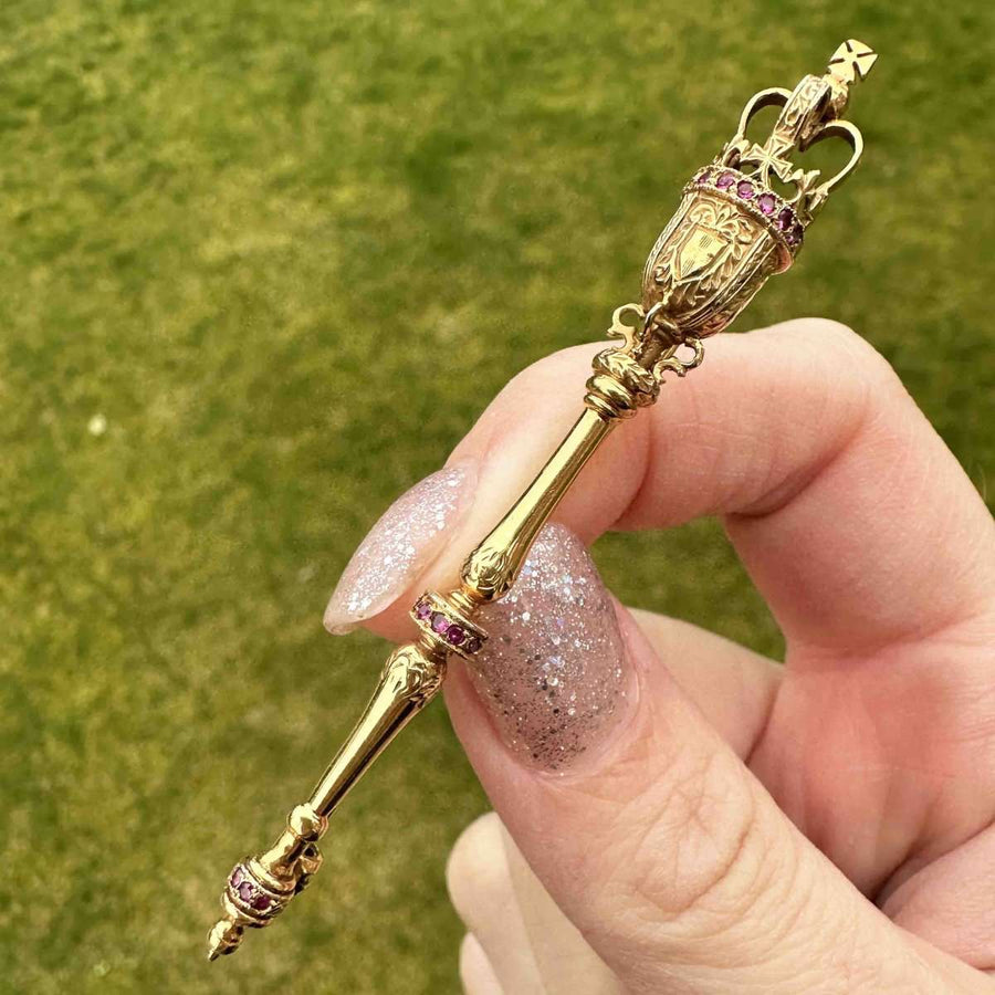 Vintage 9ct gold royal mace brooch with rubies held in hand, showcasing intricate detail and craftsmanship.