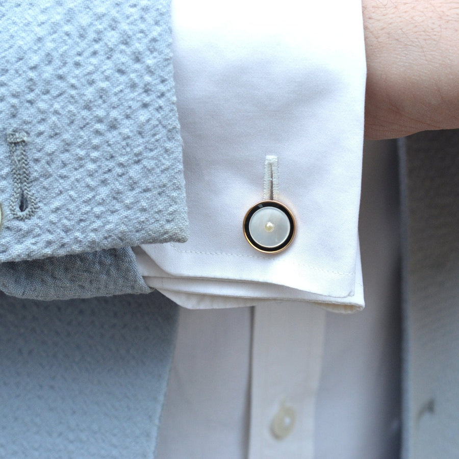 Elegant gold and pearl cufflink accentuating a white shirt cuff with a stylish grey jacket.