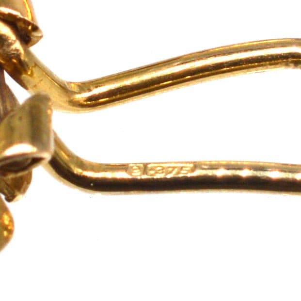 Close-up of 1940s 9ct gold flower clip-on earrings showcasing hallmark detail.