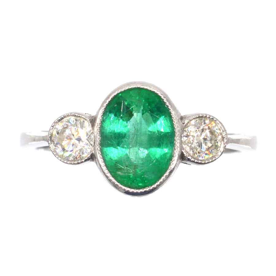 1950s platinum ring featuring a 1 carat apple green emerald flanked by two bright diamonds, perfect for vintage engagement or anniversary.
