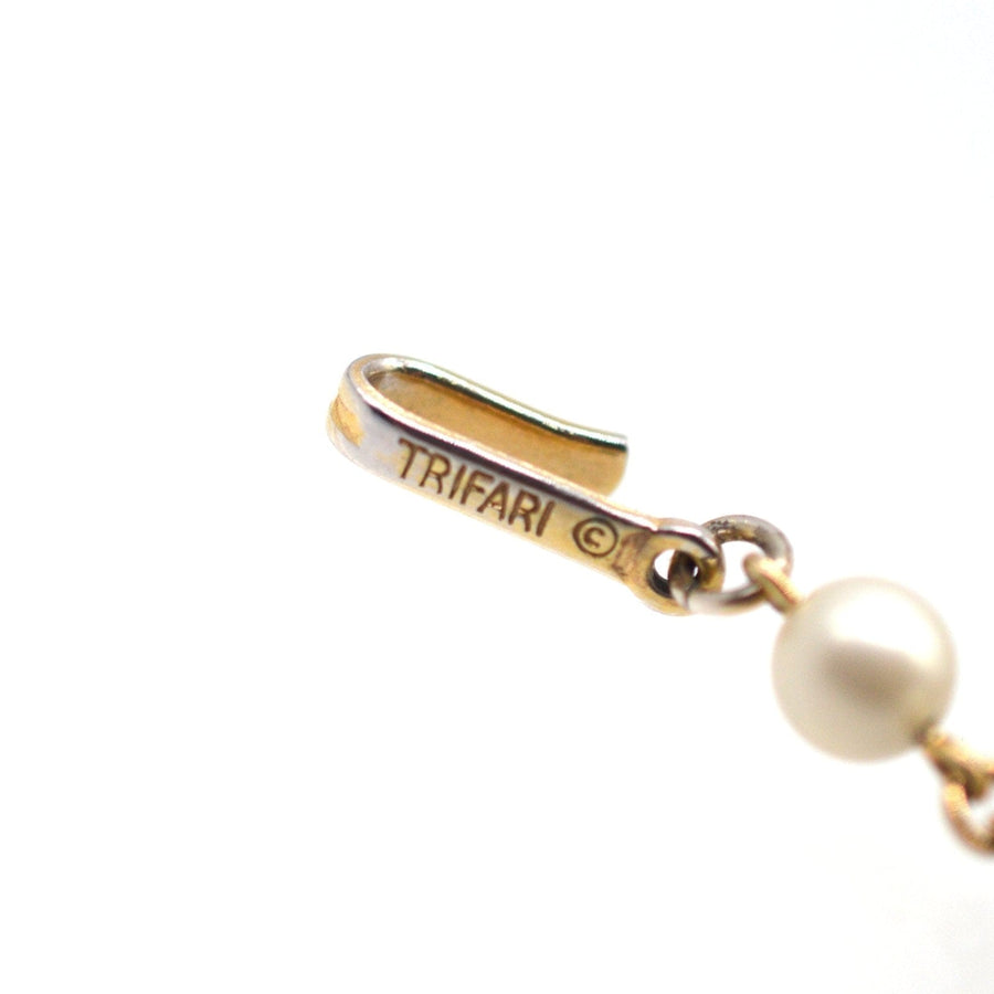 Close-up of Trifari jewelry clasp showing logo and faux pearl details.