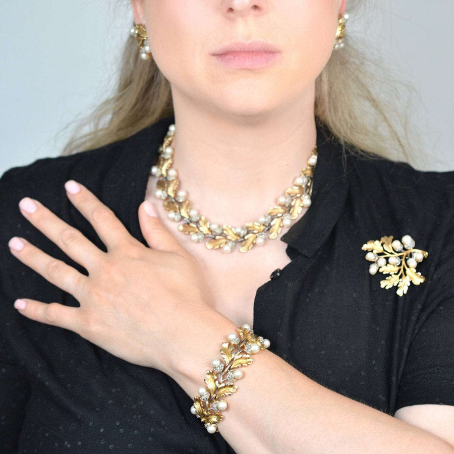 1950s Trifari gold-tone oak leaf parure with faux pearl acorns: necklace, bracelet, earrings, and brooch displayed on model.