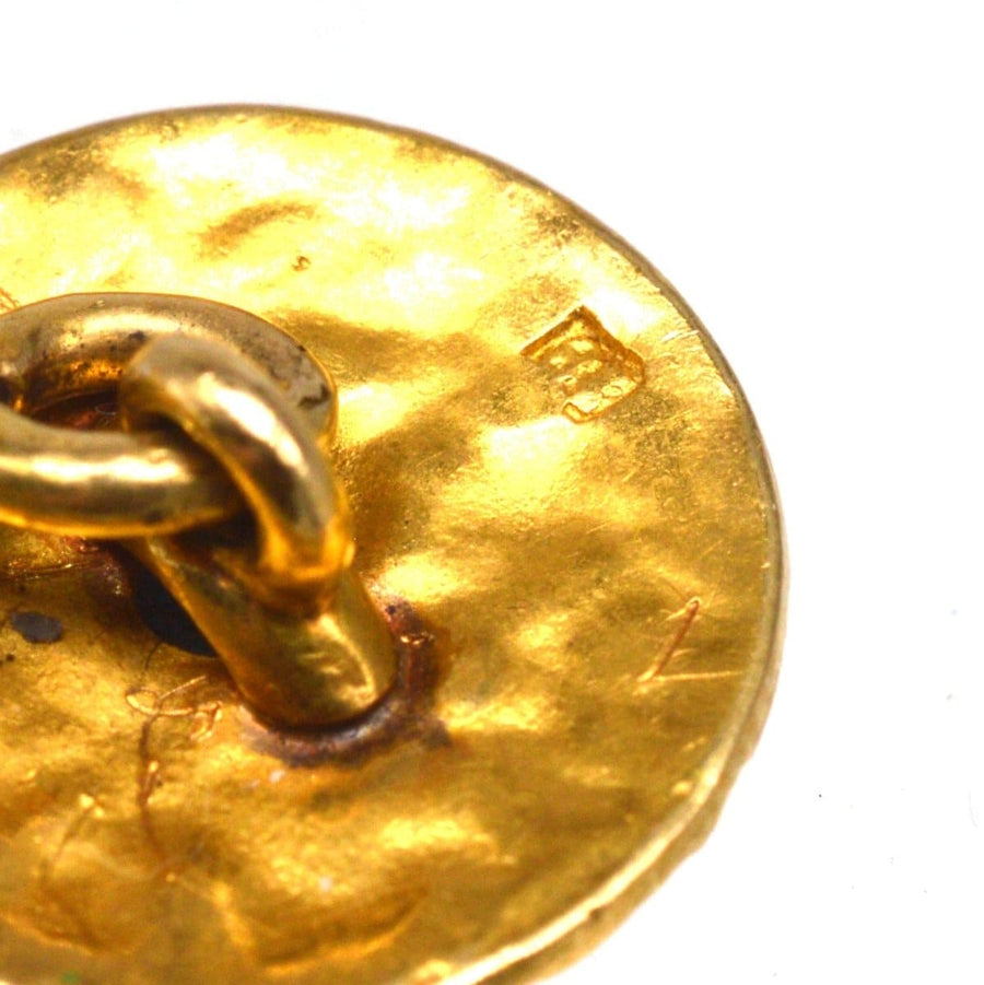 Close-up of a textured gold cufflink showcasing the hallmark and chain link detail.