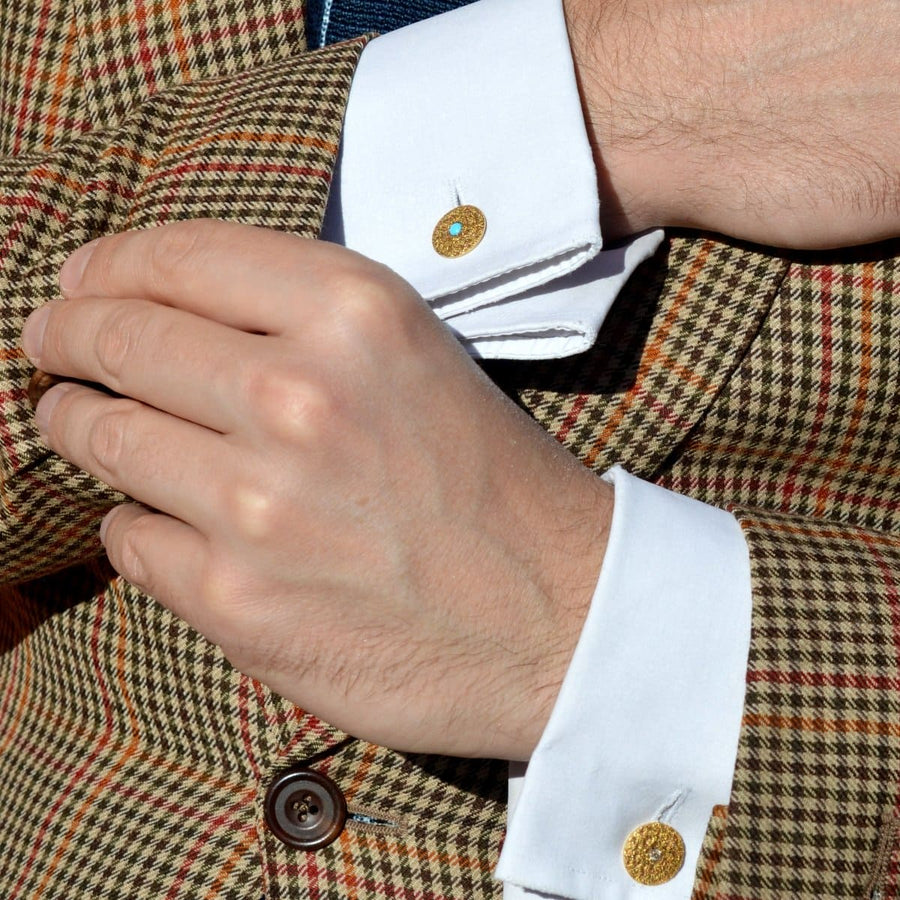 Close-up of a man wearing 1960s gold cufflinks with turquoise, complemented by a stylish checked blazer.