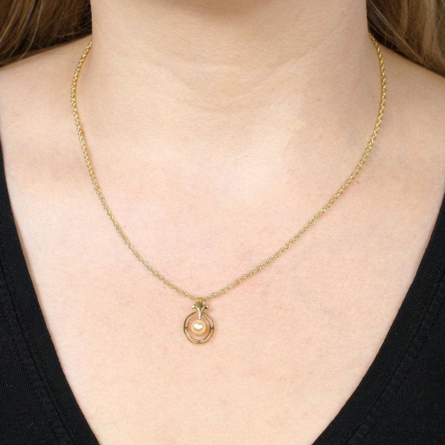 1970s 9ct gold pendant featuring cultured pearl and fleur-de-lis detail, worn on a delicate chain.