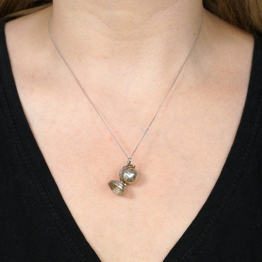 1970s silver antique globe charm pendant worn on a black shirt, showcasing its spinning feature.