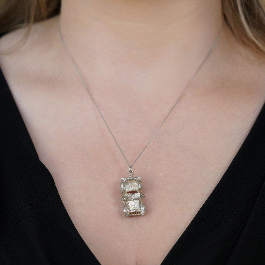 Silver vintage car charm pendant worn on a necklace, showcasing intricate detailing and movable wheels.