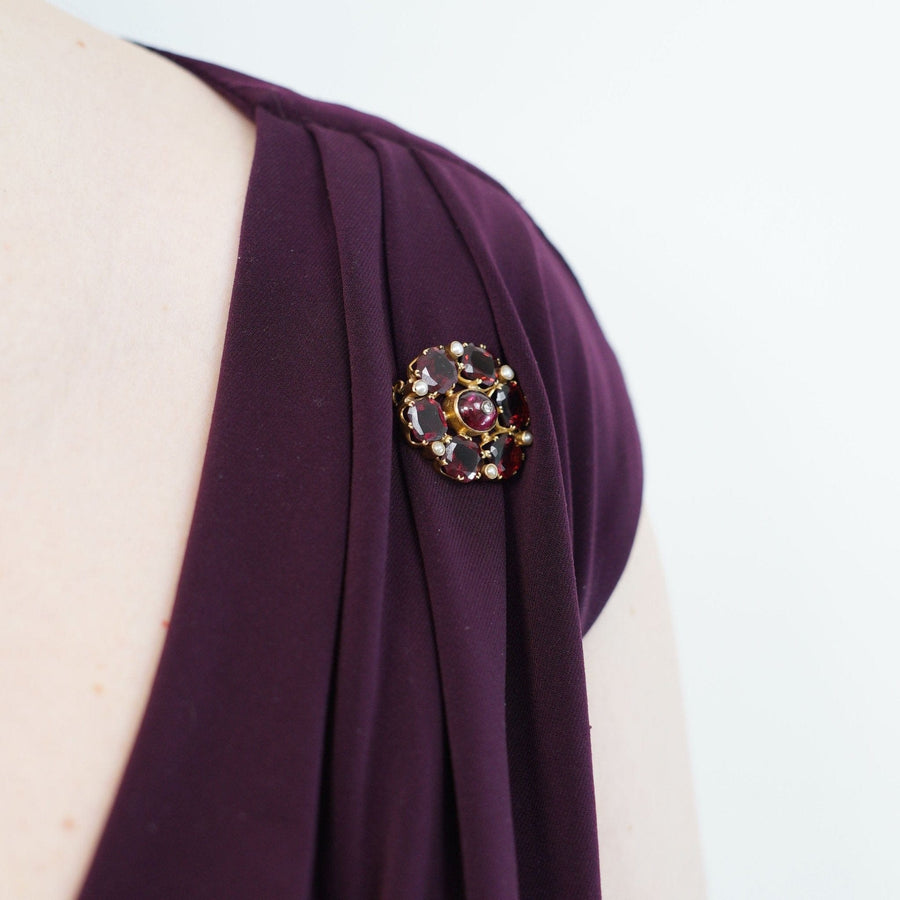 19th century 18ct gold garnet, pearl and diamond brooch worn on a purple dress shoulder.