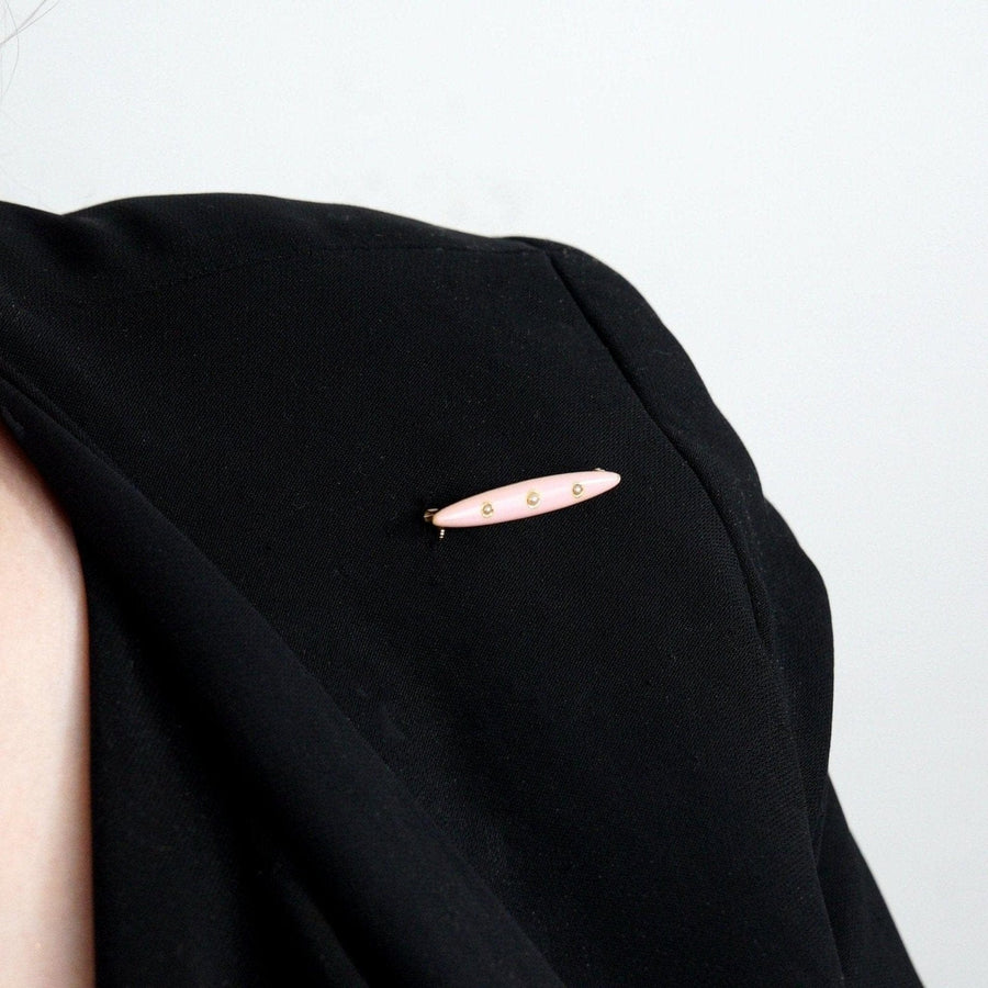American Edwardian 14ct gold bar brooch with pink enamel and three split pearls worn on a black top.