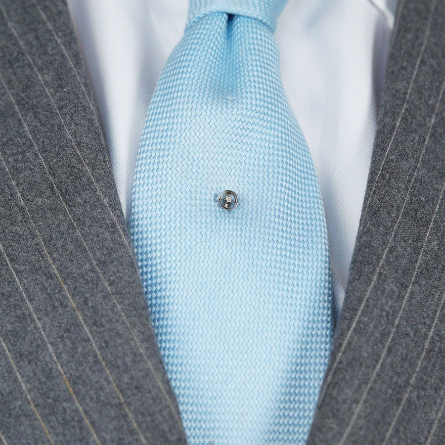 Art Deco 14ct white gold tie pin with diamond on a light blue silk tie, set against a gray striped suit.