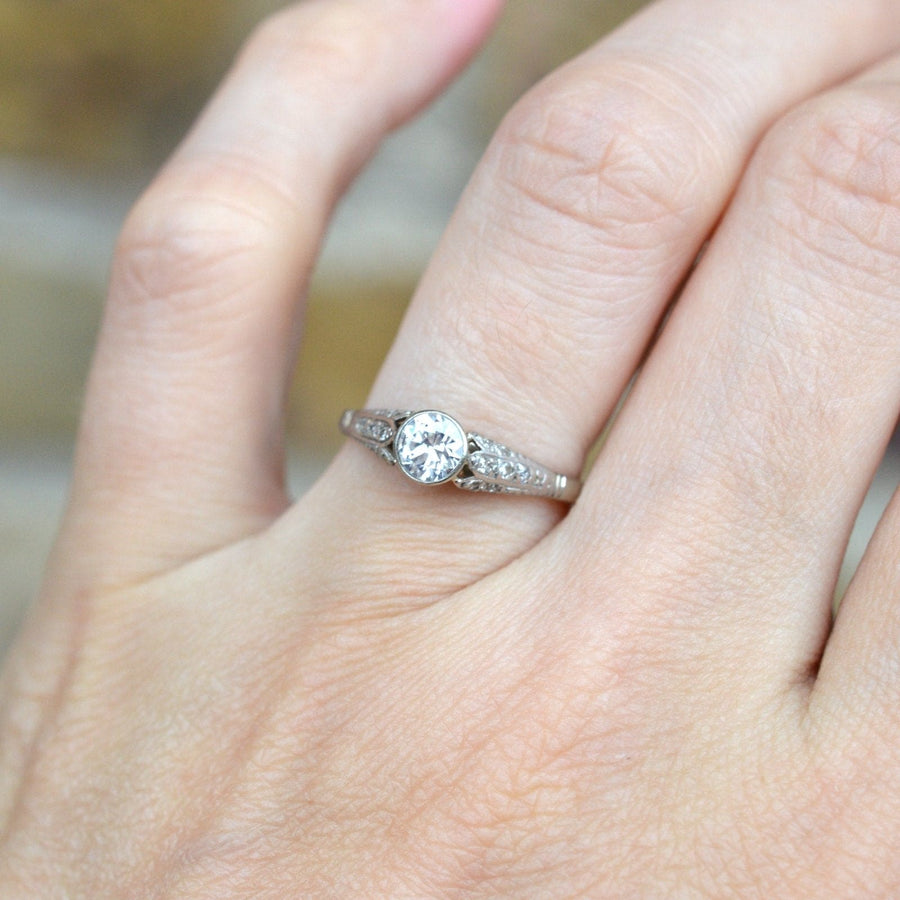 Art Deco 18ct gold and diamond solitaire ring showcased on a hand, featuring a central diamond and decorated shoulders.
