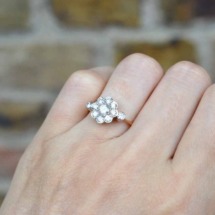 Art Deco 18ct gold and platinum diamond cluster ring on a finger, featuring a central diamond surrounded by eight smaller diamonds.