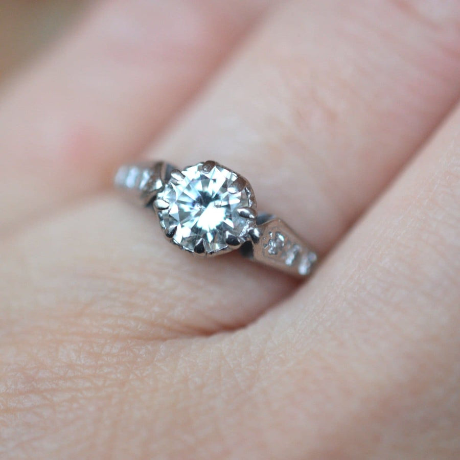 Art Deco 18ct gold and platinum diamond solitaire ring with diamond shoulders on a finger.