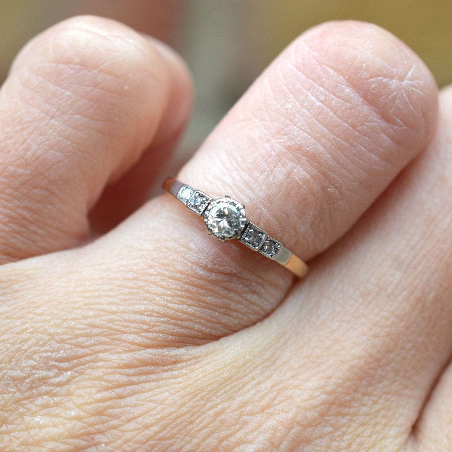 Art Deco 18ct gold and platinum diamond solitaire ring with diamond shoulders on a hand.