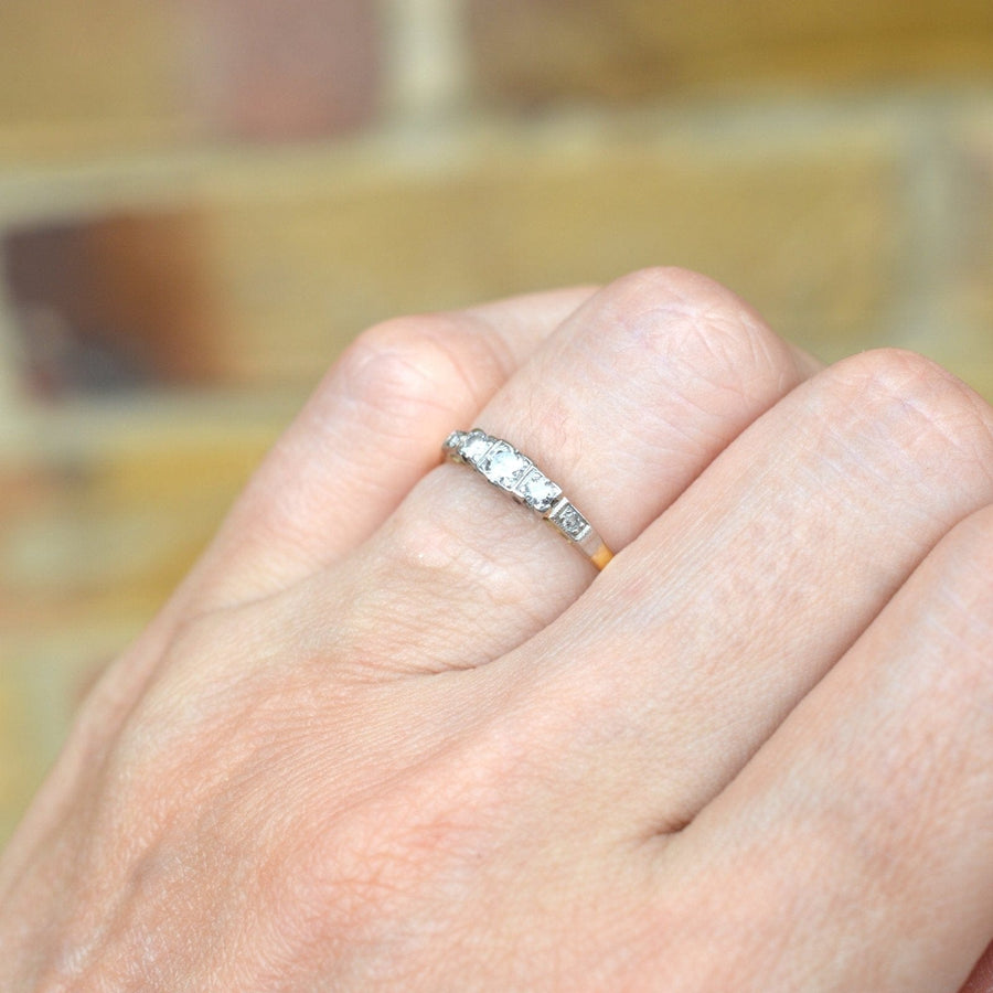 Art Deco 18ct Gold & Platinum three stone diamond ring with diamond shoulders showcased on a hand.