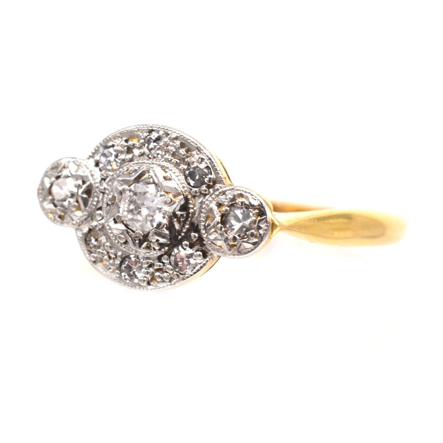 Art Deco 18ct gold and platinum three stone diamond halo ring with intricate detailing and sparkling diamonds.
