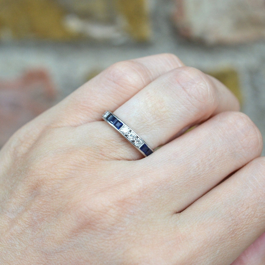 Art Deco 18ct white gold sapphire and diamond eternity ring worn on a hand against a brick background.