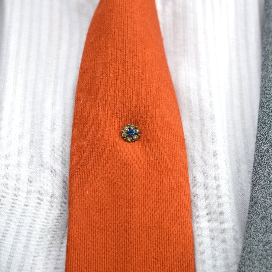 Art Deco blue and white paste cluster tie pin on an orange tie, adding elegance to formal attire.