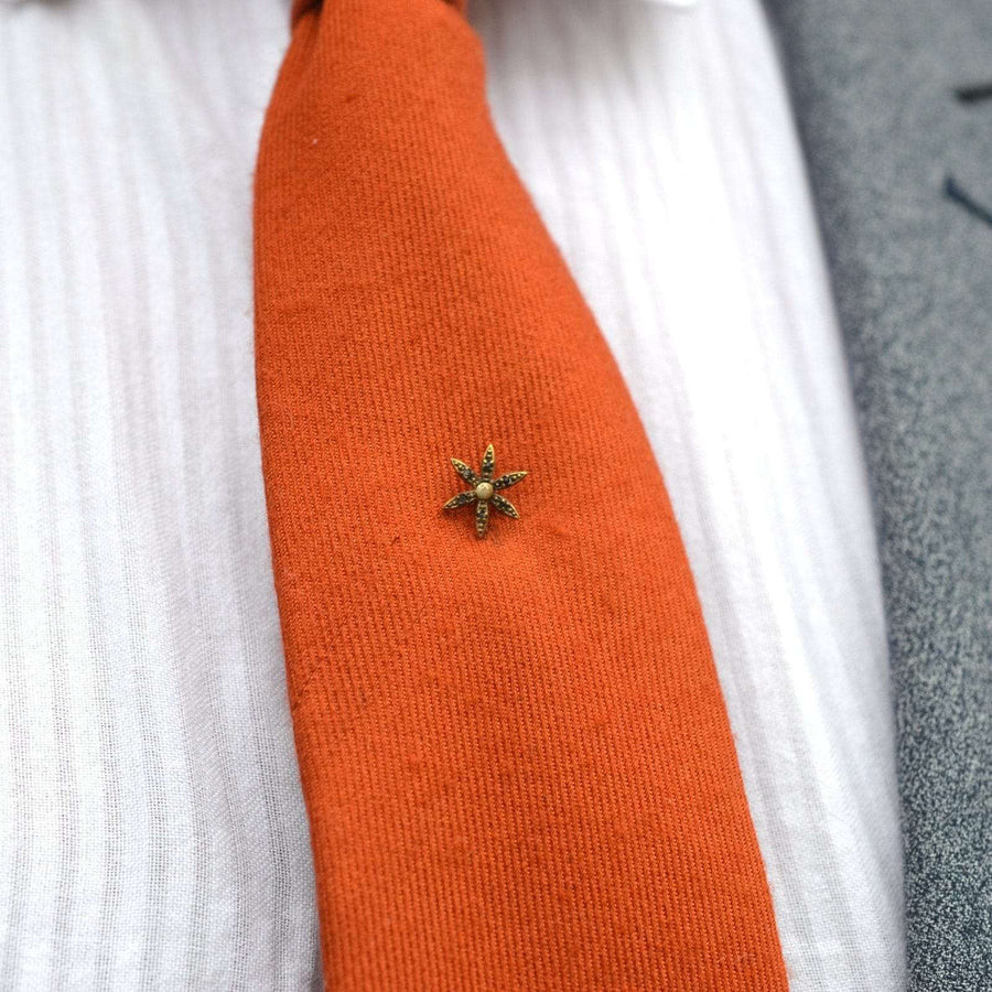 Art Deco flower tie pin featuring glass accents on orange tie, ideal for elegant formal wear.