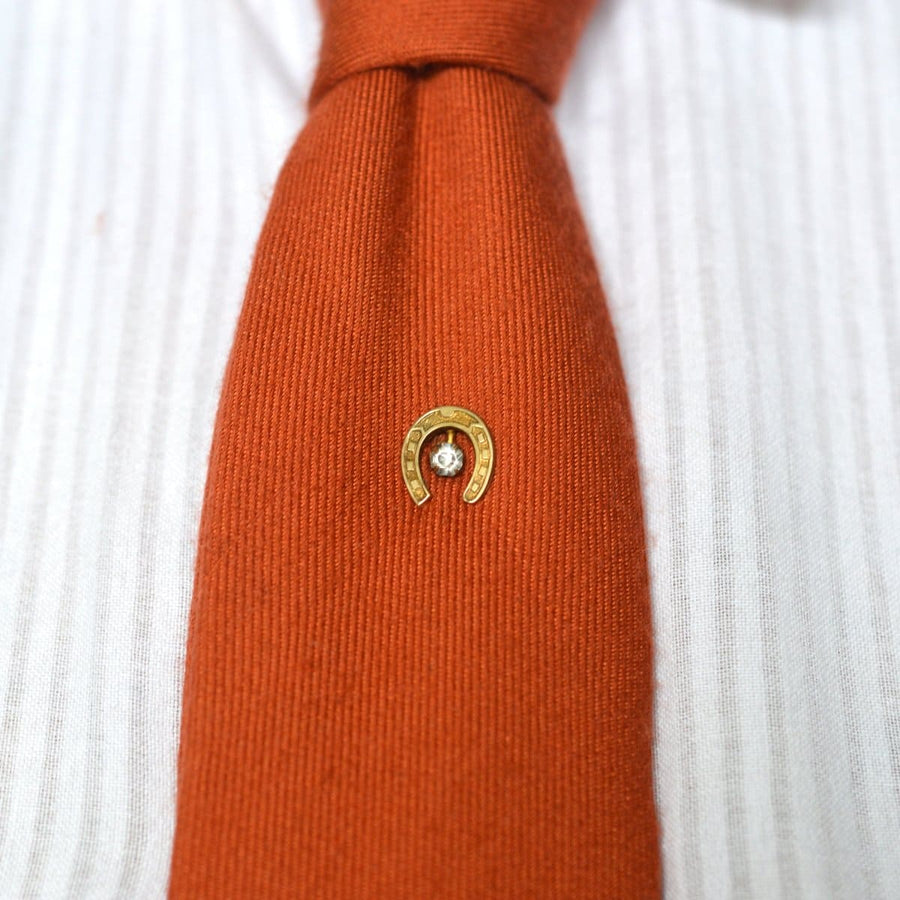Art Deco horseshoe tie pin with clear paste on an orange tie, symbolizing luck and protection.