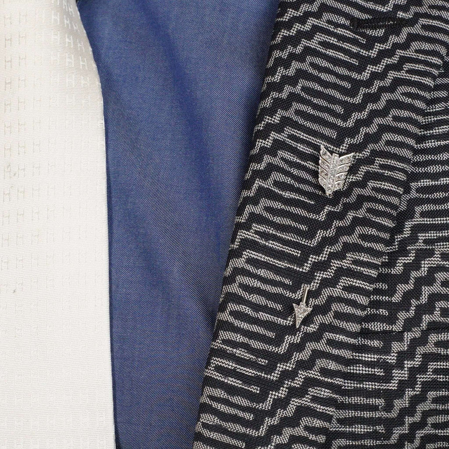 Art Deco platinum and gold arrow jabot pin brooch against patterned fabric in shades of black, blue, and white.