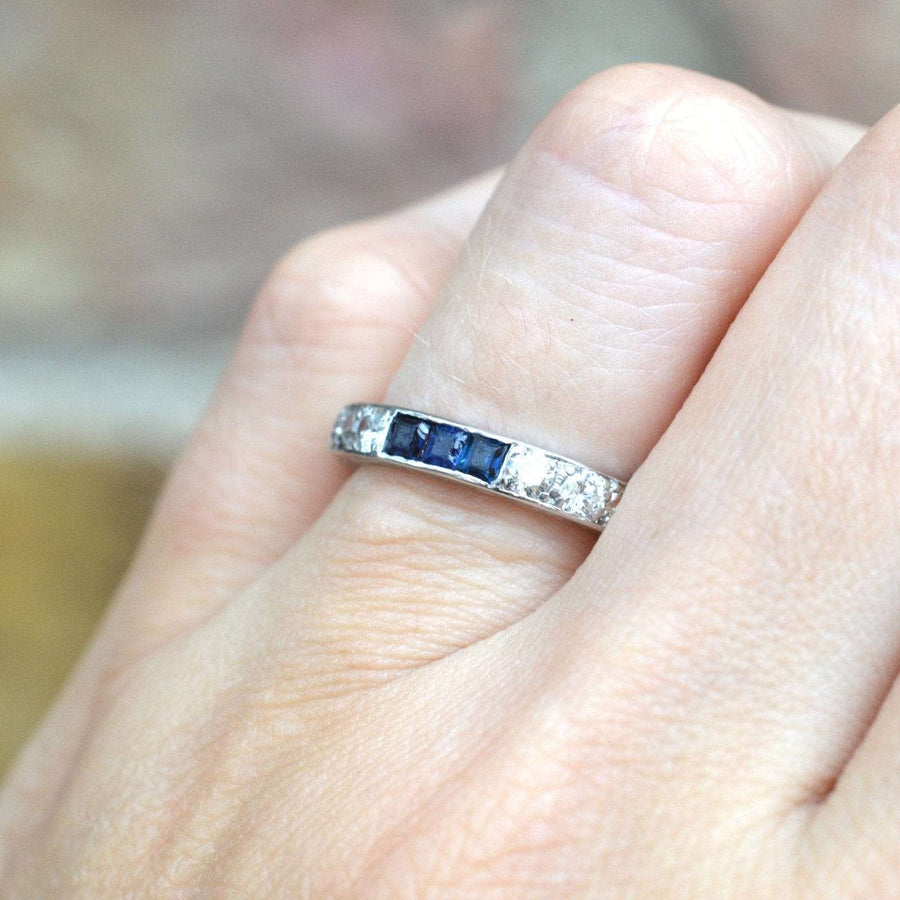 Close-up of an Art Deco platinum eternity ring featuring sapphires and diamonds, worn on a hand.