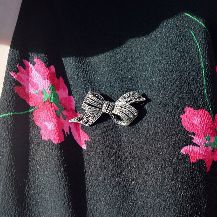 Art Deco silver and marcasite bow brooch on a floral background, showcasing vintage elegance and intricate design.