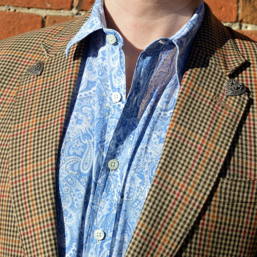 Close-up of a man wearing a patterned brown blazer with paisley shirt and decorative lapel pins.