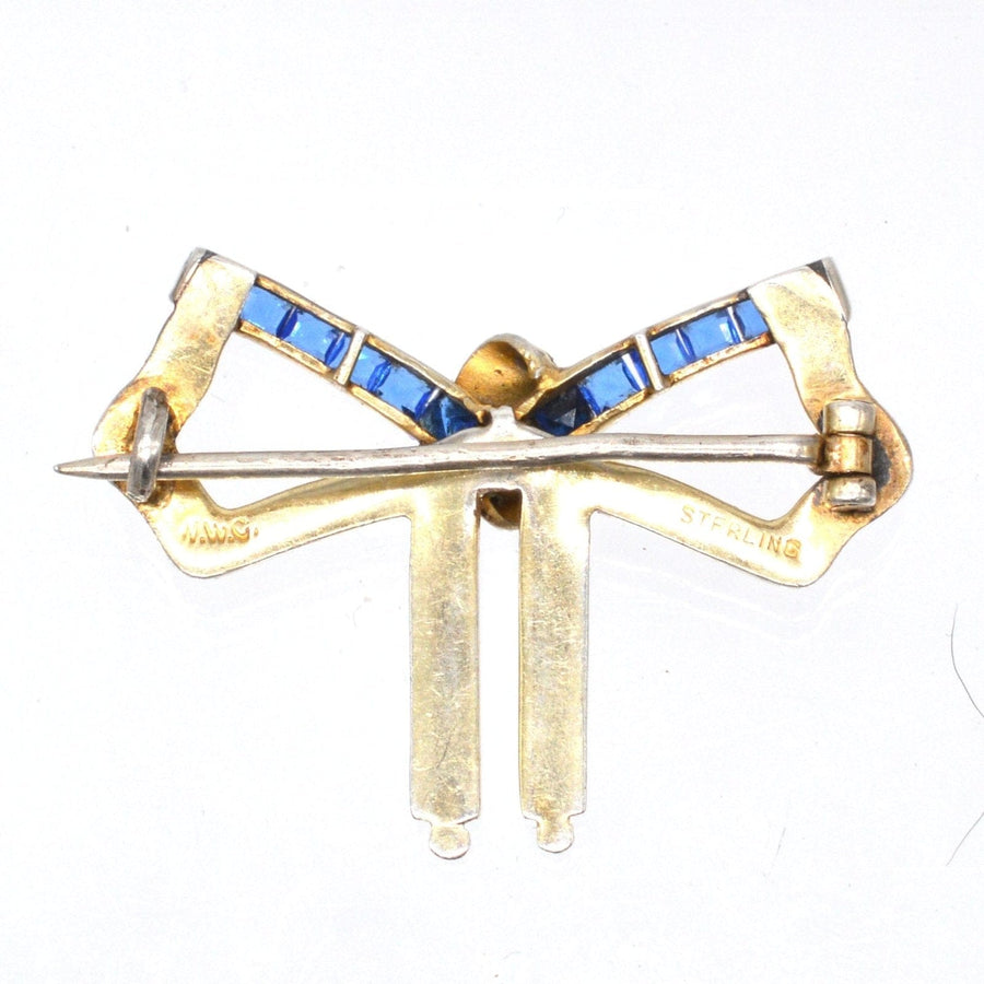 Art Deco silver and white enamel bow brooch with blue sapphire paste details, showcasing vibrant design and classic elegance.