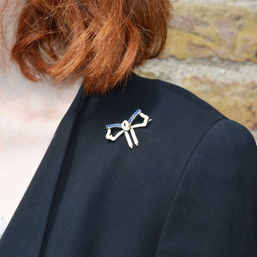 Art Deco silver bow brooch with blue paste accents worn on a black jacket, showcasing vibrant design.