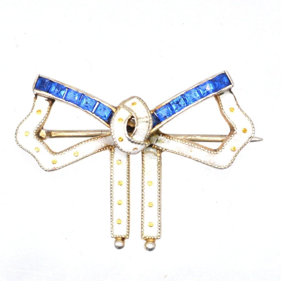 Art Deco silver and white enamel bow brooch with blue sapphire paste detailing, showcasing elegant design and vibrant colors.