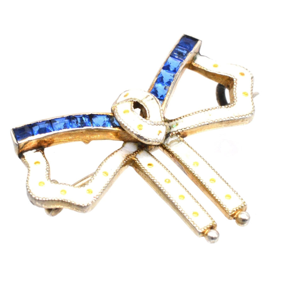 Art Deco silver and white enamel bow brooch with blue sapphire paste stones, showcasing vibrant colors and stylish lines.