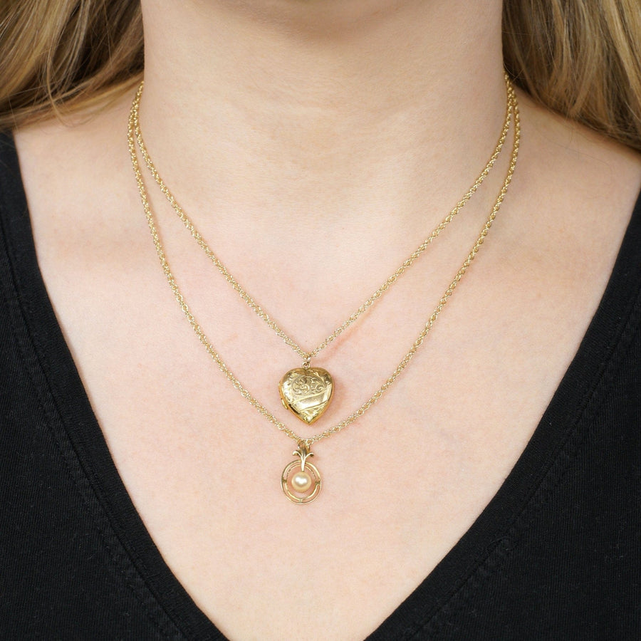 Gold layered necklaces featuring a heart pendant and circular charm, worn on a black top.