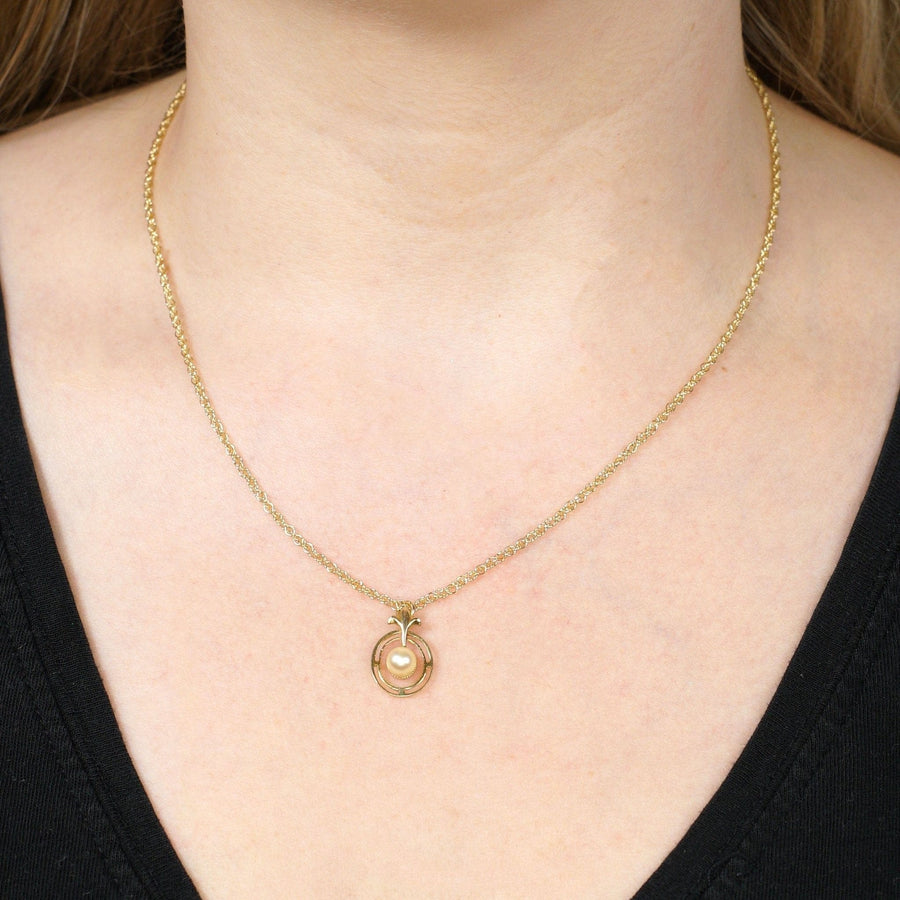 Gold necklace with a circular pendant worn on a person, showcasing fine jewelry design and elegant style.