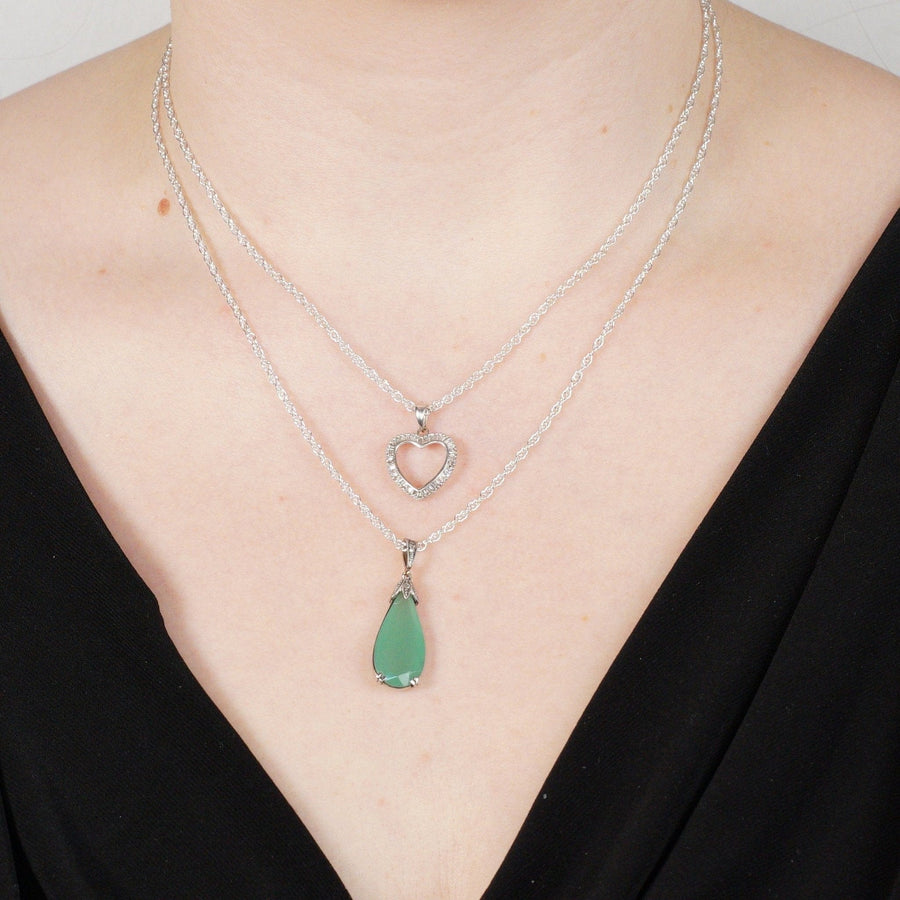 Layered silver necklaces featuring heart and green teardrop pendants on a model's neck, stylish and elegant jewelry.