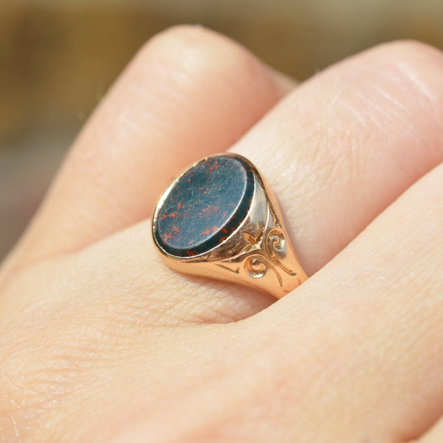 Edwardian 15ct gold bloodstone signet ring worn on hand, showcasing intricate design and polished stone surface.