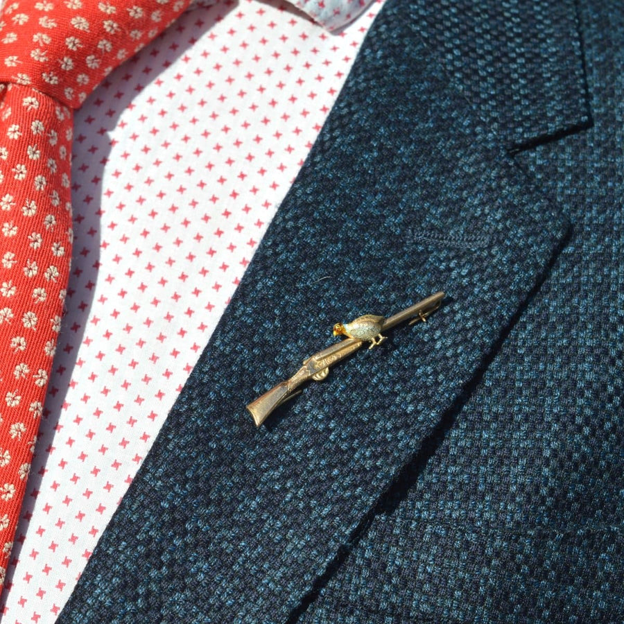 Edwardian brooch featuring a gold grouse on a shotgun, set on a stylish blazer lapel.