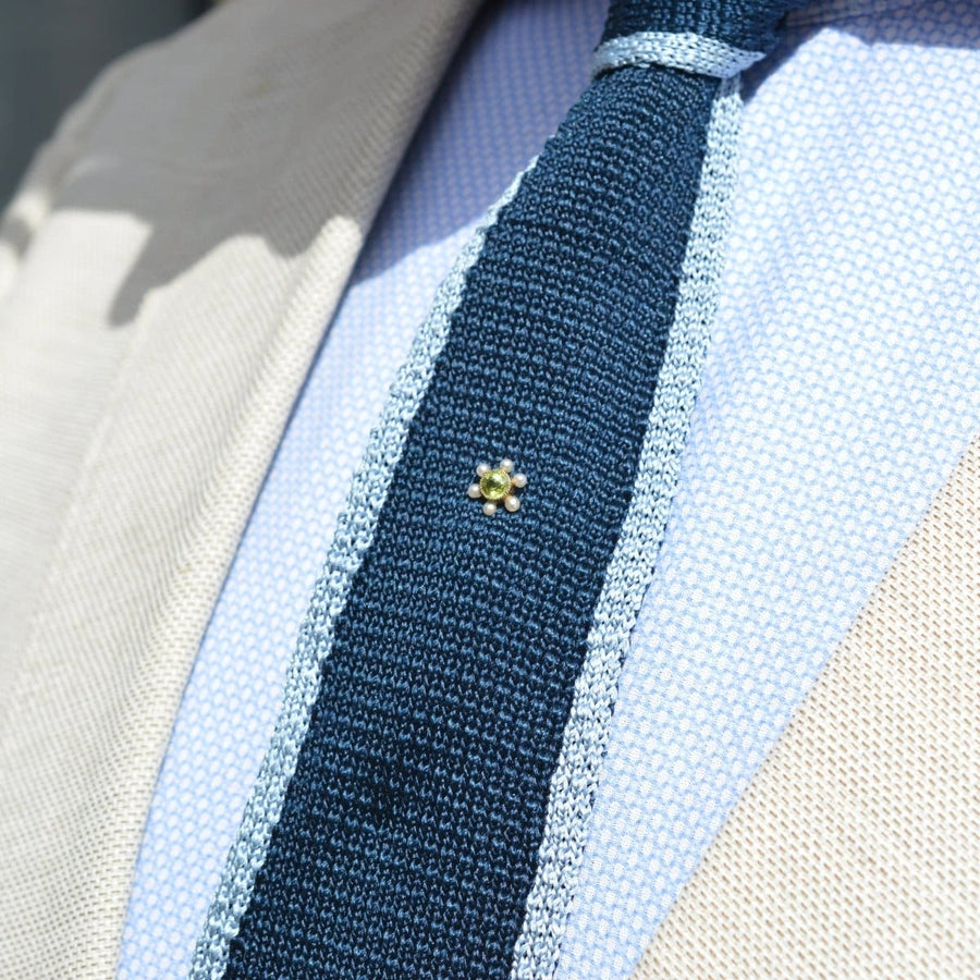 Edwardian gold peridot and pearl tie pin on a silk tie, showcasing classic jewelry design.
