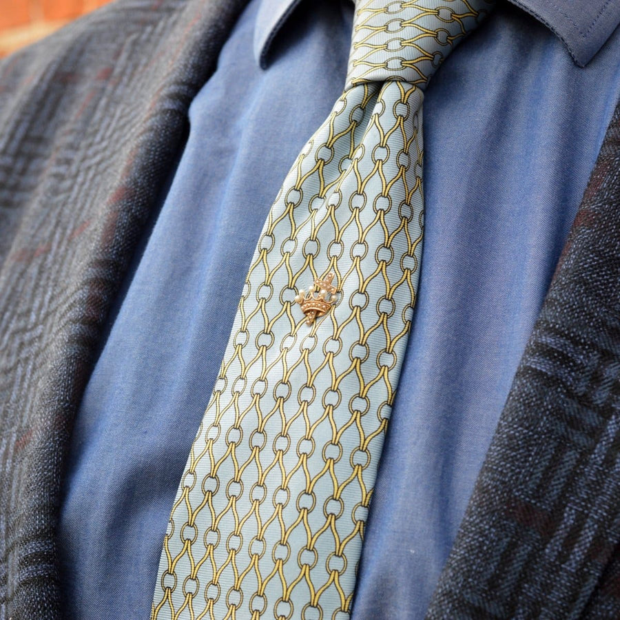 Elegantly styled tie with a gold tie pin featuring a cross and crown design, perfect for formal occasions.