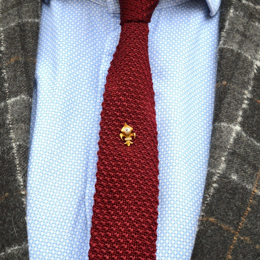Edwardian 18ct gold Fleur de lys tie pin on a textured burgundy tie, stylishly paired with a patterned blazer.