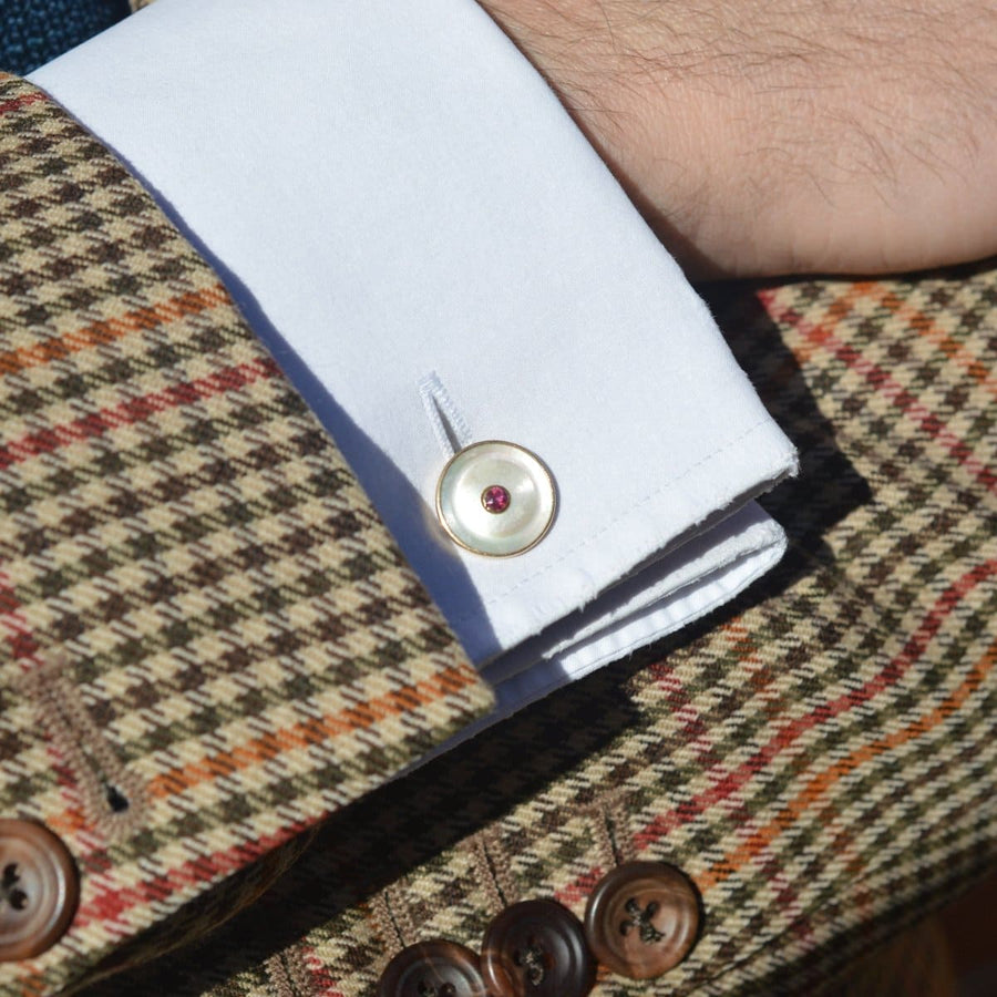 Close-up of Edwardian cufflinks with ruby and mother of pearl on a patterned jacket sleeve.