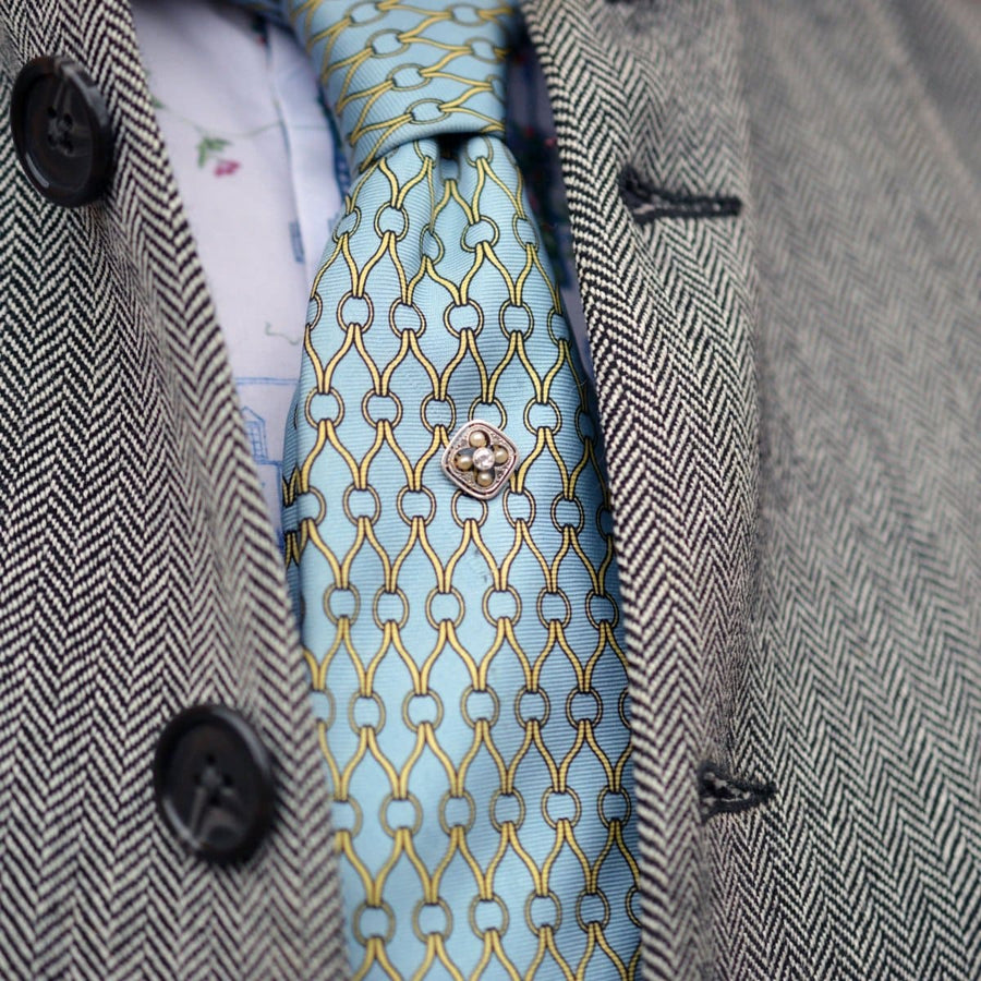 Elegant blue patterned tie with a metallic tie pin, complemented by a herringbone jacket.